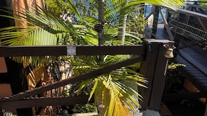 A wooden gate with a number sign, a palm tree, and a stone pathway. - Suítes Azul Marinho (Ilhabela)