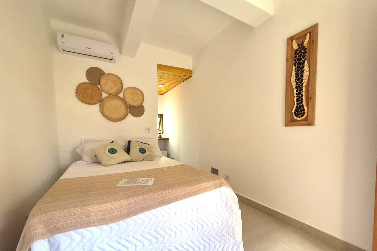 Ein Schlafzimmer mit einem Bett, einer wandmontierten Klimaanlage, einer gewebten Wanddekoration und einem gerahmten Kunstwerk.