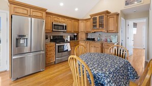 A kitchen with wooden cabinets, stainless steel appliances, and a dining area with a patterned tablecloth. - Reeds beach retreat 2 bedroom with water view (Reeds Beach)