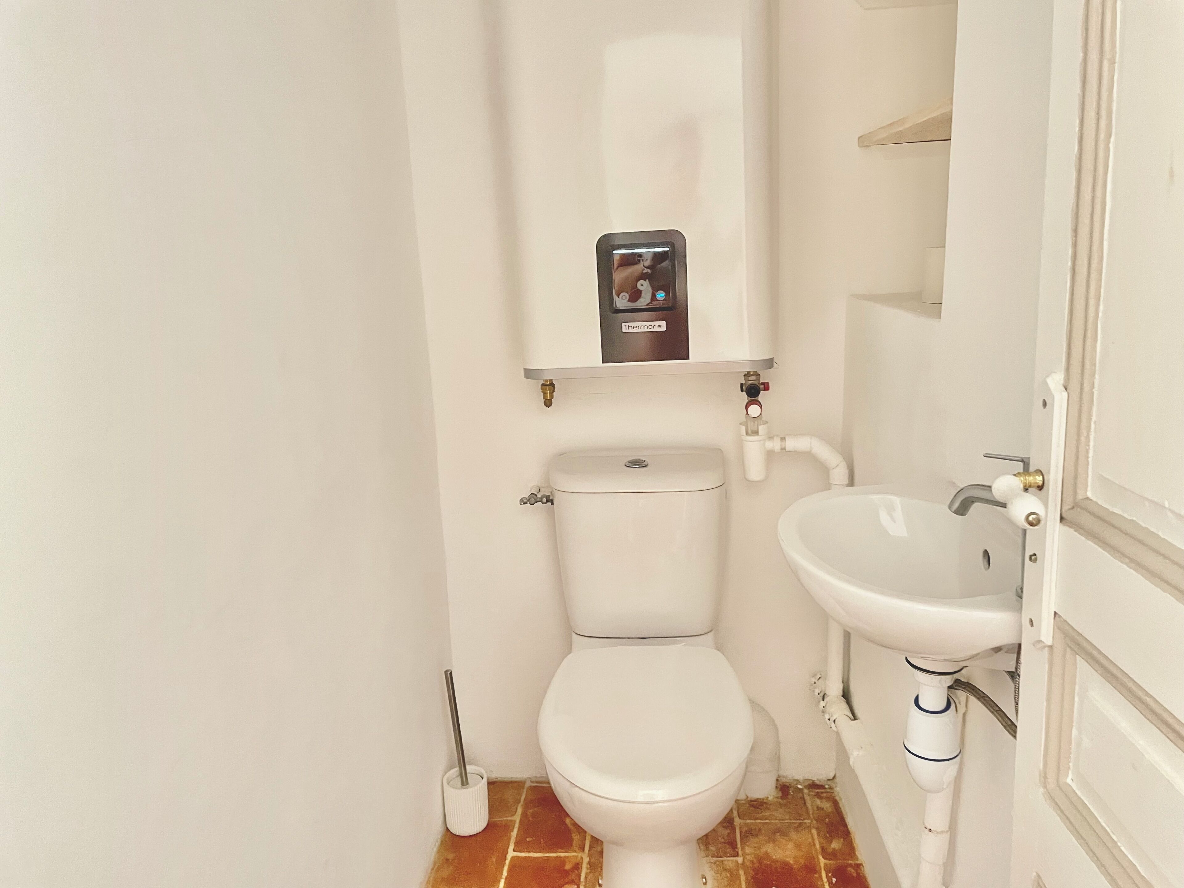 Un baño pequeño y blanco con inodoro, lavamanos y dispensador de papel higiénico.