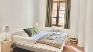 A neatly made bed with a white comforter and green pillows, a bedside lamp, a window with curtains, and a radiator.