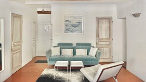 A living room with a teal sofa, white coffee table, and a white armchair. There is a painting on the wall and a wooden beam ceiling.