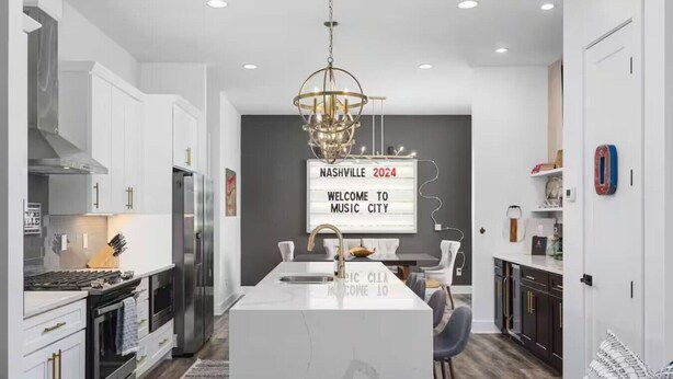 A modern kitchen with a central island, stainless steel appliances, and a chandelier.