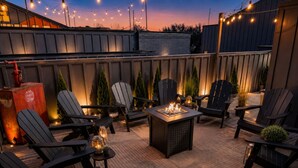 An outdoor patio with Adirondack chairs, a fire pit, and string lights.
