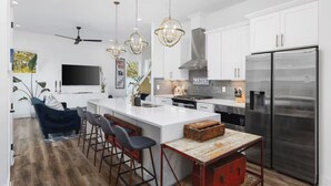 A modern kitchen with white cabinets, a stainless steel refrigerator, and a bar area with stools.