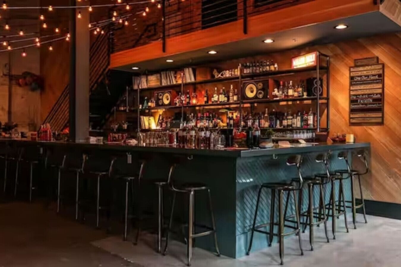 A bar area with a long counter, multiple stools, and a variety of bottles and glasses.