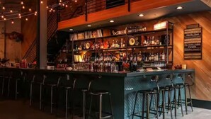 A bar area with a long counter, multiple stools, and a variety of bottles and glasses.