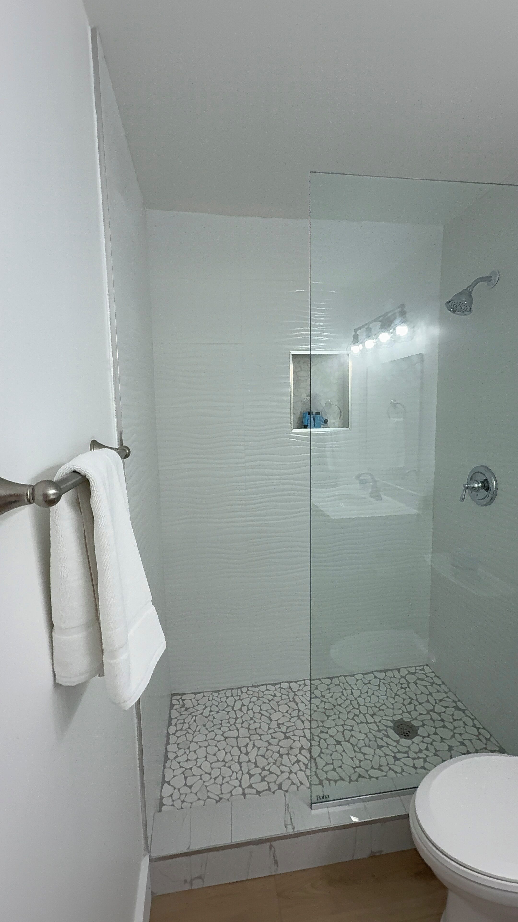 Une douche fermée par des parois de verre, avec un sol carrelé, des toilettes et un porte-serviettes avec des serviettes.