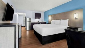 Una habitación de hotel con una cama grande, un escritorio, un televisor de pantalla plana, un refrigerador y un microondas.