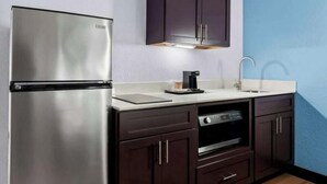 Una cocina compacta con un refrigerador de acero inoxidable, armarios de madera oscura, un horno empotrado y un lavamanos con un grifo moderno.