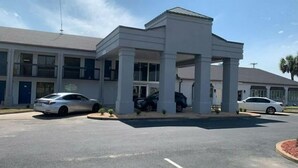 Un motel con zona de estacionamiento techada, varios coches aparcados y cielo despejado.