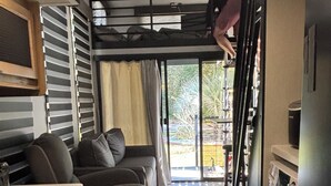 A compact living space with a kitchenette, a sofa, a dining table, and a bunk bed. - Timberwolf in the Park (Pensacola)