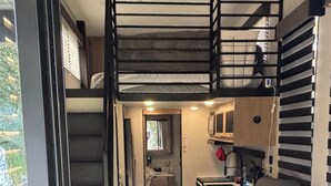 A compact RV interior with a kitchenette, a sofa, a dining area, and a staircase leading to an upper level. - Timberwolf in the Park (Pensacola)