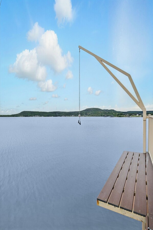 A wooden deck with a swing overlooking a calm body of water and distant hills.