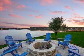 A lakeside patio with blue Adirondack chairs and a fire pit.