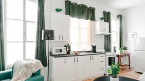 Cocina compacta con alacenas blancas, microondas, estufa y pileta. Hay una mesa de comedor con una planta encima.