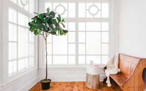 Une pièce avec une grande fenêtre, un banc en bois, une plante en pot et une petite table blanche.