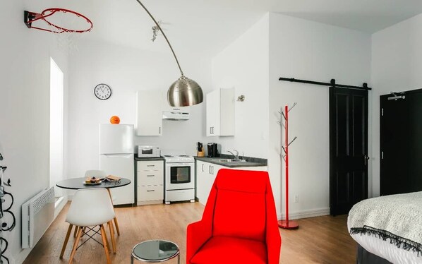 Un espace de vie compact comprenant un coin cuisine, un coin repas et une chaise rouge.