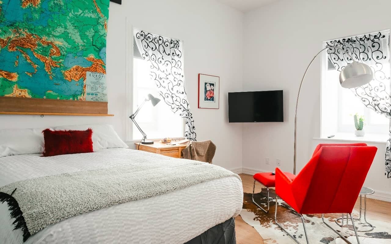 A bedroom with a bed, a desk, a chair, a TV, and a map on the wall.