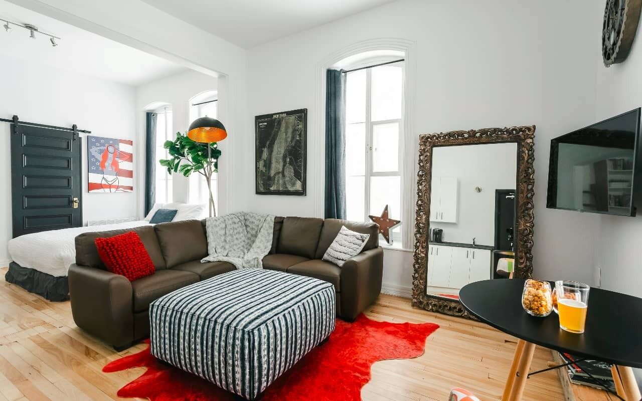 A modern living room with a sofa, ottoman, and a dining table with glasses and snacks.