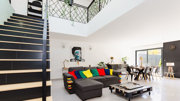 Una sala de estar moderna con un sofá seccional gris, cojines coloridos, una mesa de centro y una escalera con barandales negros.