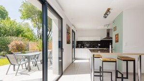 Una cocina moderna con una isla grande, puertas de cristal correderas que dan a un patio exterior y un comedor con mesa y sillas.