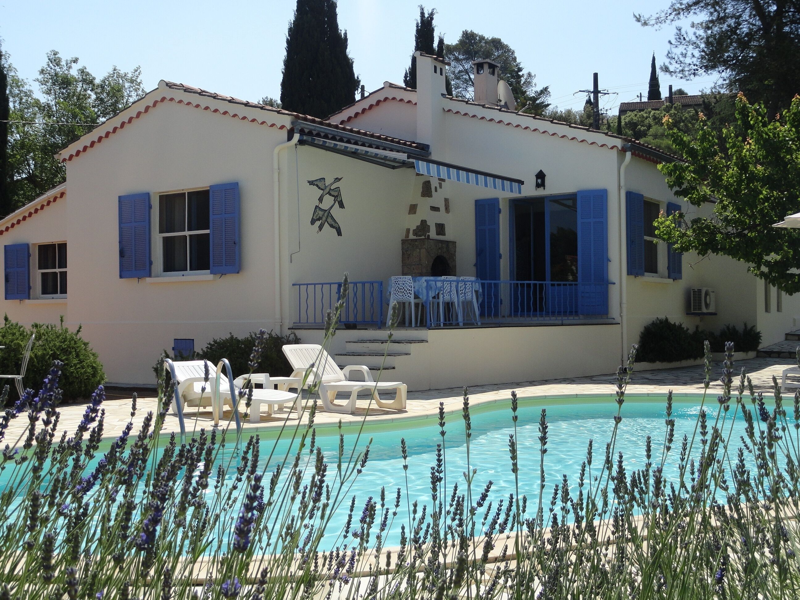 Un bâtiment doté d’une piscine, de murs blancs, de volets bleus et d’un balcon avec des chaises blanches.