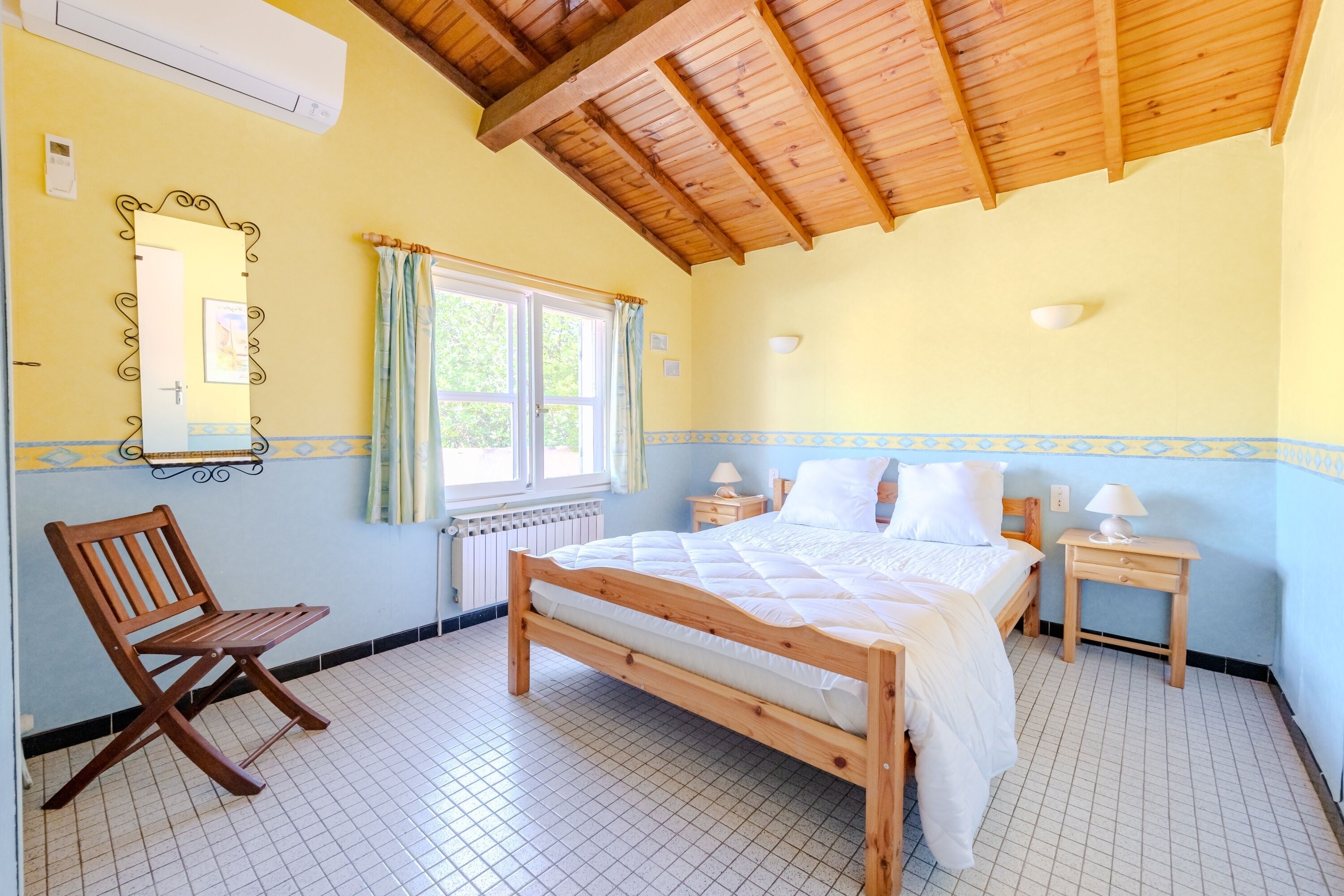 A bedroom with a wooden bed, a chair, a window with curtains, and a radiator.