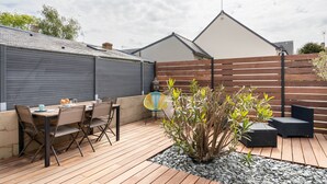 A patio with a table and chairs, surrounded by a wooden fence and plants. - Le Repos des Vagues - 4min de la Plage (Dinard)