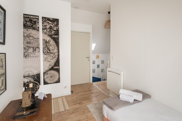 A bedroom with a wooden floor, a bed with white bedding, a desk with a vintage typewriter, and two wall-mounted posters of a globe.