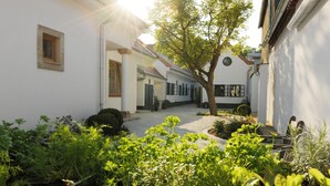 A courtyard with a paved path, surrounded by white walls and greenery. - Hotel Genuss am Hof (Halbturn)