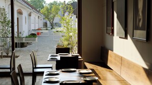 An outdoor dining area with tables and chairs, a pathway leading to a building, and a view of a street with buildings and trees. - Hotel Genuss am Hof (Halbturn)