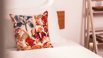 A neatly made bed with a floral pillow, a wooden headboard, and a white wall with a small light fixture.