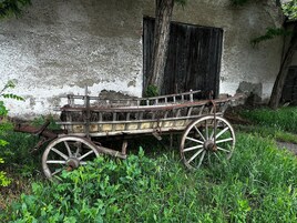 Un viejo carruaje de madera con ruedas de metal, estacionado junto a una pared desgastada con una ventana.