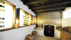 A wine cellar with wooden shelves displaying bottles, a brick wall, and a fireplace. - Hotel Genuss am Hof (Halbturn)