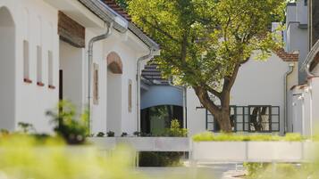 A white building with a tree in front, a blue awning, and a white fence.