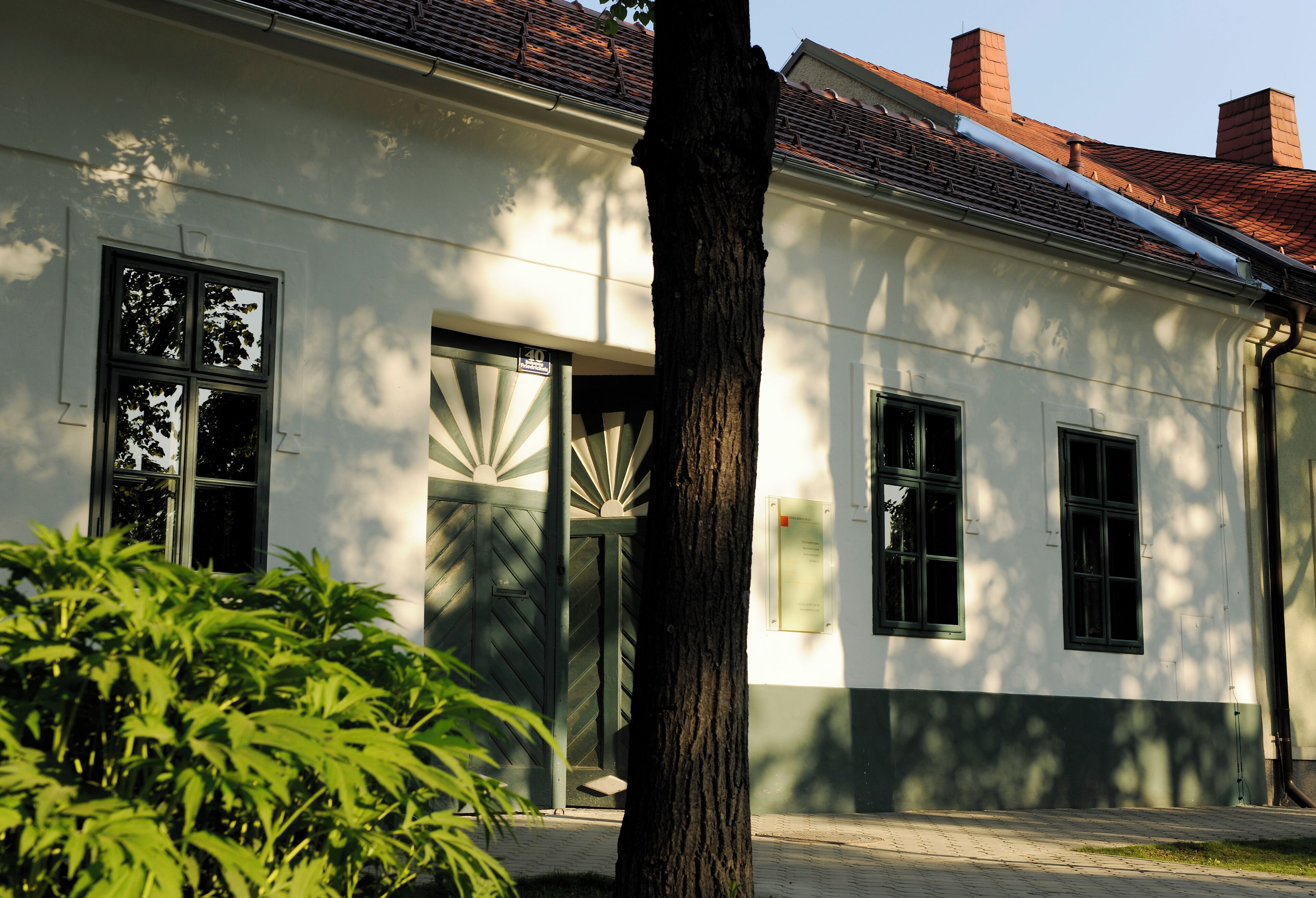 Un bâtiment blanc à l’architecture traditionnelle, doté d’une grande fenêtre et d’une porte ornée d’un motif en verre en forme d’éventail.