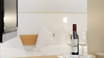 Habitación de hotel con cama, mesita de noche con una botella de vino y copas, y televisor instalado en la pared.