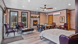 Una habitación amplia con una cama grande, una mesa de comedor y varias sillas. Tiene una chimenea, un ventilador de techo y ventanas amplias.