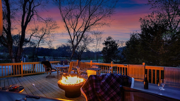 Una terraza con asientos exteriores, una fogata y vistas a árboles y al atardecer.