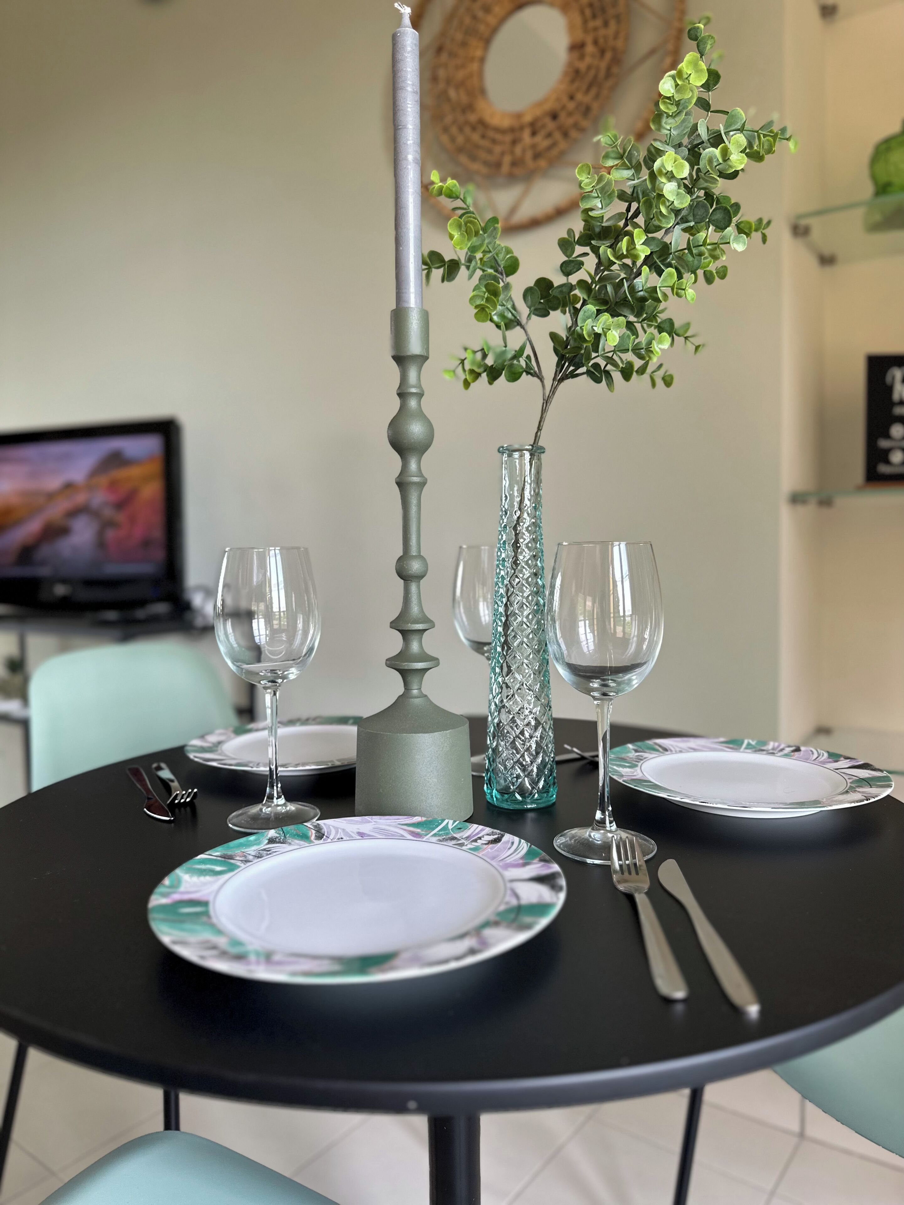 A dining table set with plates, glasses, cutlery, and a decorative vase with greenery.