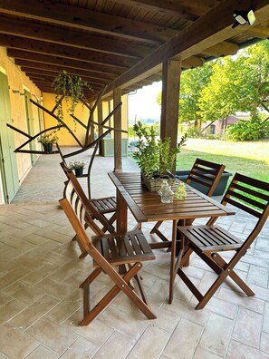 A covered patio with a wooden table and chairs, potted plants, and a view of the garden. - Just Langhe Casa Dolcetto (Piemonte)