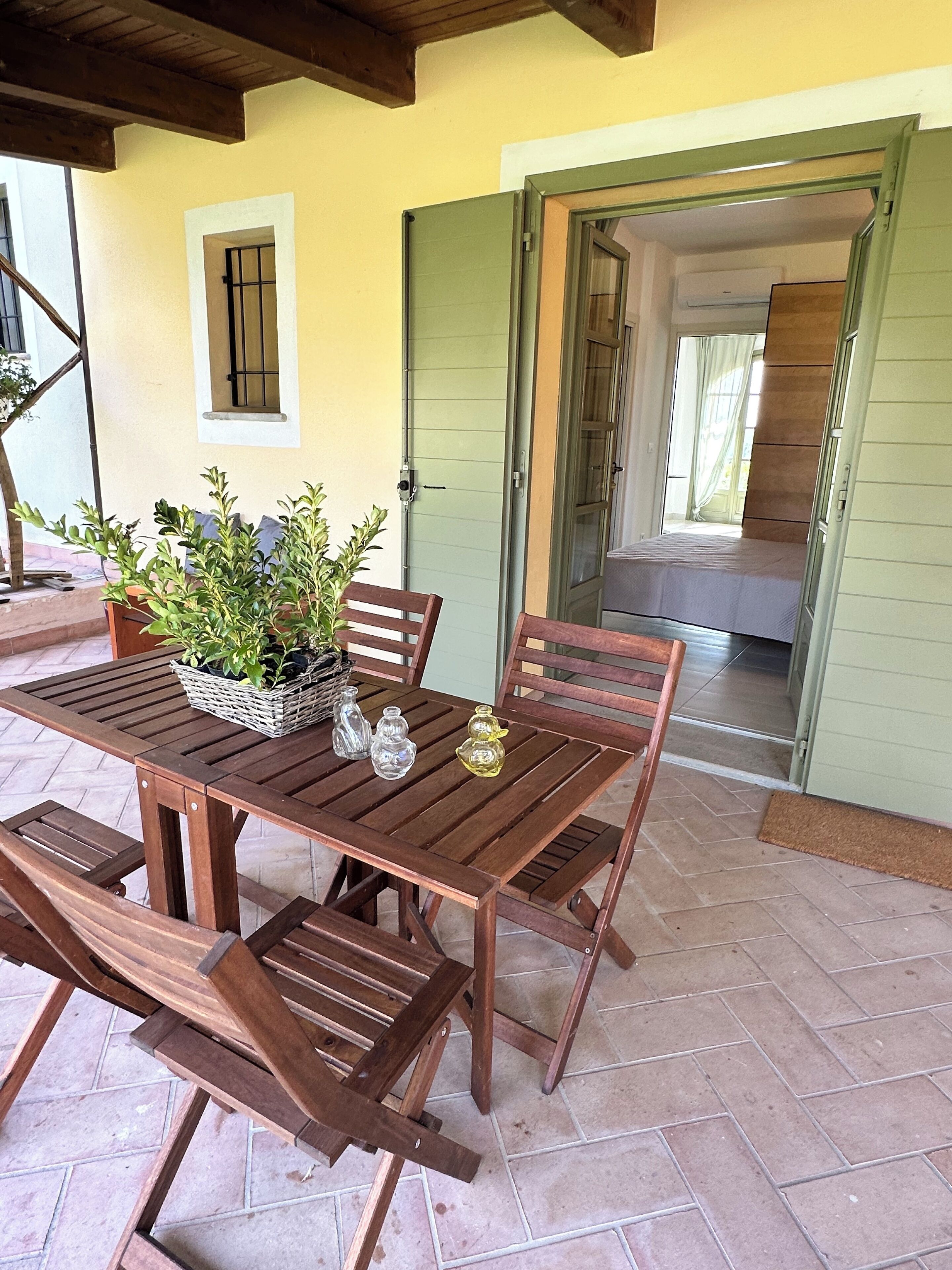 A wooden patio table with benches, a potted plant, and decorative glassware.