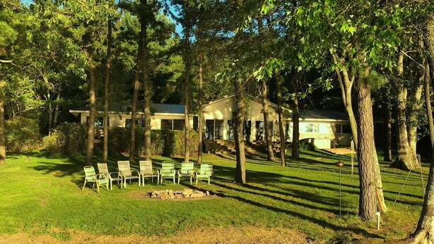 A building surrounded by trees, with a grassy area and several chairs arranged in front.