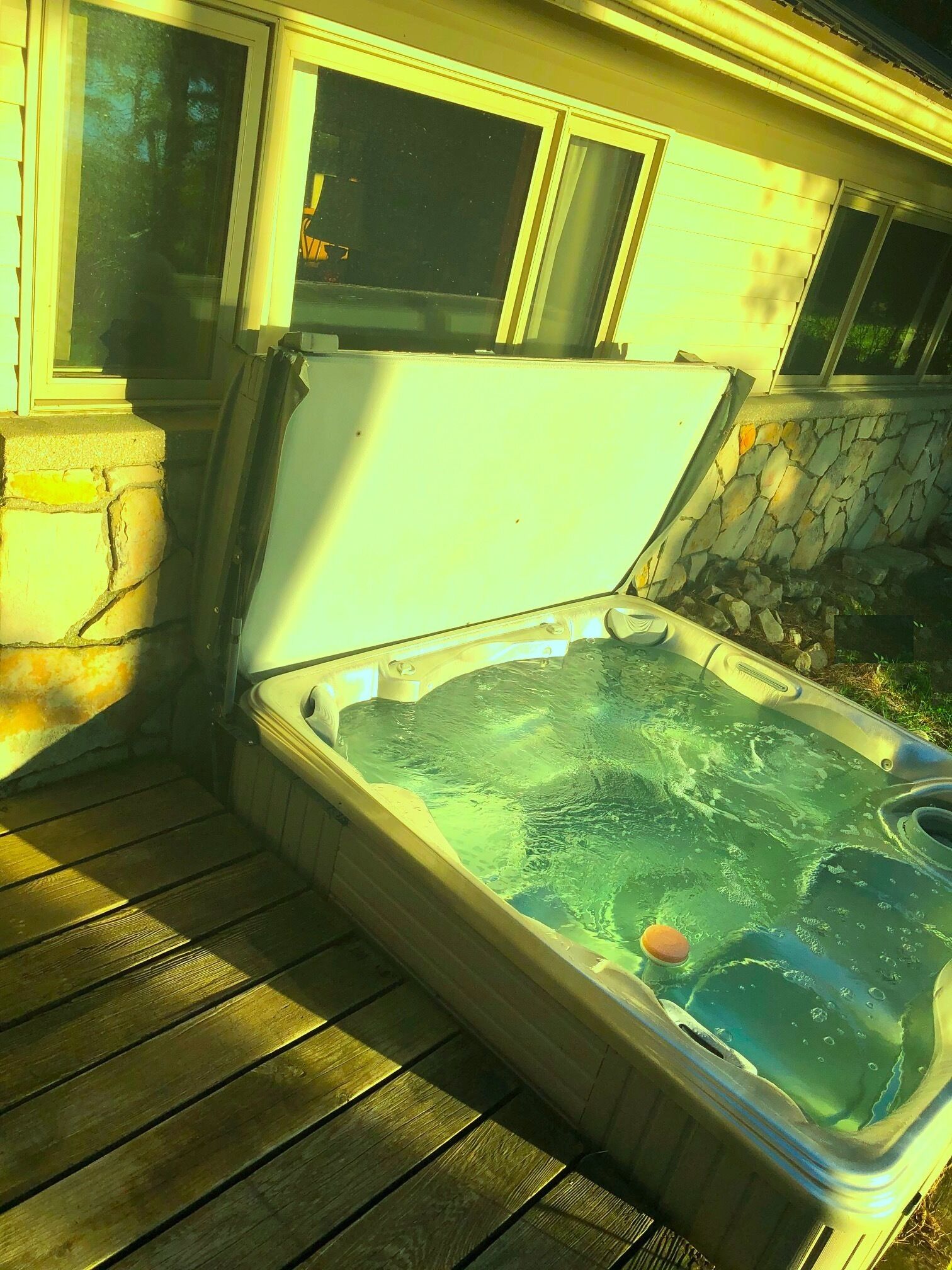 Un bain à remous avec un mur en pierre et une terrasse en bois.