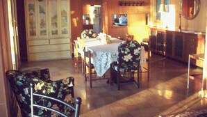 A dining area with a table set for four, surrounded by floral-patterned chairs. There is a cabinet with glass doors and a television on a stand.