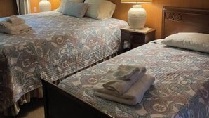 A hotel room with two beds, each with a patterned bedspread and pillows, a nightstand with a lamp, and wooden paneling on the walls.
