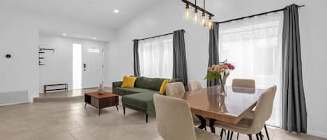 Una sala de estar moderna con zona de comedor, que incluye un sofá, una mesa de centro y una mesa de comedor con sillas.