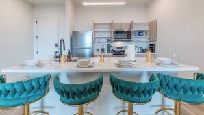 A modern kitchen with white countertops, stainless steel appliances, and teal bar stools.