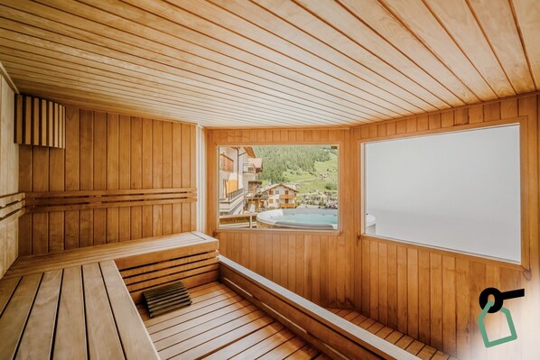 A wooden sauna room with a large window offering a view of a pool and buildings. - Hotiday Bormio Valdidentro (San Carlo)